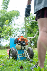 Gardener carefully mowing the green lawn with a modern lawn mower on a sunny day outdoors.