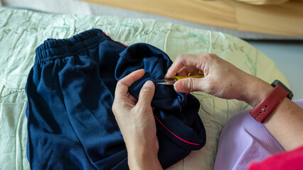 Hands of a mother sewing trouser legs, repairing her child&rsquo;s pants with patience and skill.