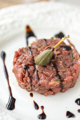 Beef tartare with caper and balsamic sauce on white plate