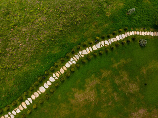 Aerial view of a winding stone path bordered by shrubs on a green lawn, creating a geometric contrast with nature.