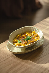 Bowl of soup with dumplings and fresh herbs on wooden table