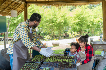 A happy farmer family working in hydroponic greenhouse farm. A man is watering seedlings with a...