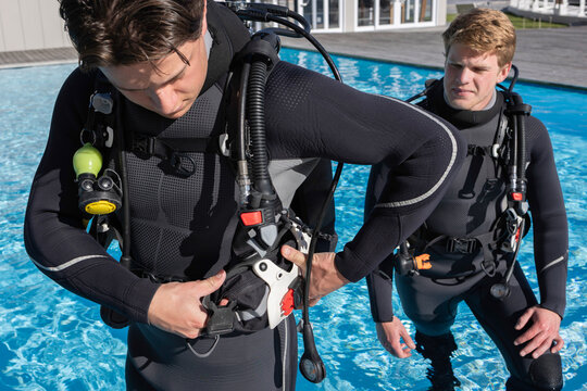 A scuba diver is getting his gear ready by inserting a weight pocket into his BCD pocket&mdash;two divers in a pool at a dive resort.