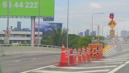 A view of an expressway under construction in Bangkok, marked by cones, directional signage, and billboard advertisements in the background.
