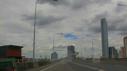 A quiet elevated highway stretch in Bangkok, with modern skyscrapers in the distance and light poles lined along the expressway.