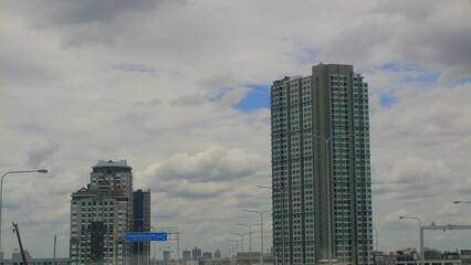 Cluster of high-rise buildings seen from a city highway, highlighting Bangkok's diverse architectural styles and dense urban development.