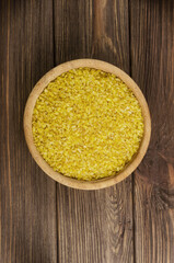 Raw bulgur wheat grains in a wooden bowl on a brown table. Healthy eating concept. Vegan and vegetarian food. Diet. Rustic style. Vertical orientation. Top view. Copy space