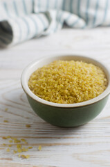 Raw bulgur wheat grains in a ceramic green bowl on a white wooden table. Healthy eating concept. Vegan and vegetarian food. Diet. Rustic style. Vertical orientation.
