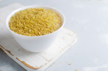 Raw bulgur wheat grains in a ceramic white bowl on a white cutting board on a gray background. Healthy eating concept. Vegan and vegetarian food. Rustic style. Horizontal orientation. Copy space