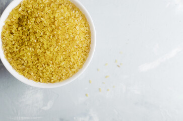 Raw bulgur wheat grains in a ceramic white bowl on a gray background. Healthy eating concept. Vegan and vegetarian food. Rustic style. Horizontal orientation. Copy space. Top view