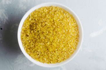 Raw bulgur wheat grains in a ceramic white bowl on a gray background. Healthy eating concept. Vegan and vegetarian food. Rustic style. Horizontal orientation. Top view