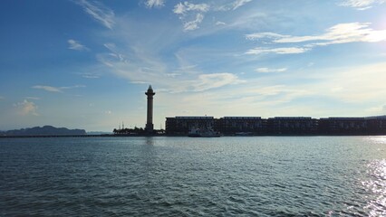 Fototapeta premium A scenic view of Ha Long City’s harbor with a lighthouse silhouetted against the afternoon sun reflecting on the water.