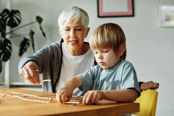 Portrait of grandmother and grandson having fun together playing board game pick-up sticks at home