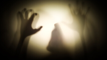 Silhouette of a hooded man with his hands raised menacingly behind a transparent curtain. Concept of demons, paranormal phenomena, ghosts, zombies.