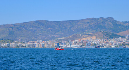 Red fishing boat floats calmly in Turkey surrounded by blue waters, gentle waves, and coastal scenery, Izmir bay, Turkey.
