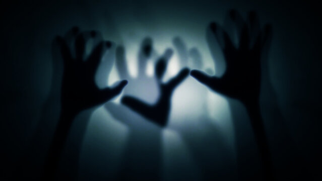 Silhouettes of many human hands behind translucent glass, curtain. The concept of the other world, victims of violence, paranormal phenomena, ghosts, zombies.