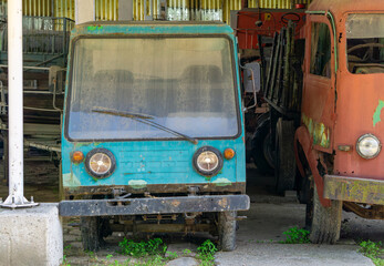 Abandoned PRL-era delivery vehicles under a shelter, covered in dust and rust.