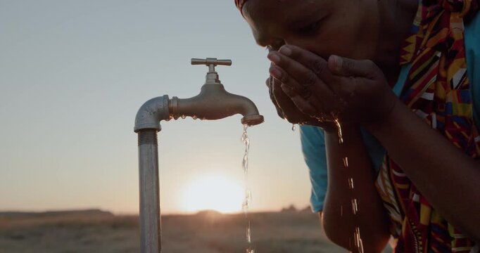 Backlit cropped close-up of a Black African woman in traditional clothing drinking water from a faucet at sunset