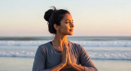 Young South Asian woman meditates in a yoga pose on a beautiful beach during a vibrant golden hour, showcasing peace and natural beauty.