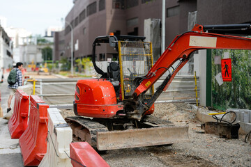 A compact orange mini excavator is parked on a construction site in an urban area © Freddy Chandra