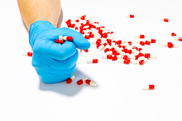 A gloved hand holds red and white pills scattered on a white surface.