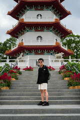 A young Asian man stands on the steps leading up to a multi-tiered traditional Chinese pagoda