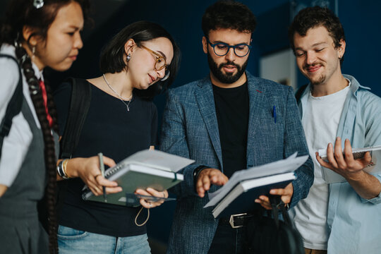 A group of college students attentively discussing academic topics with their professor in a hallway. The interaction highlights teamwork, learning, and collaboration in an educational environment. - Powered by Adobe