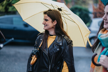 Two young women strolling through an urban setting on a rainy day, one holding a yellow umbrella,...