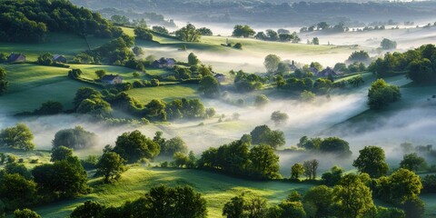 Mist gently blankets a lush, green countryside with rolling hills, scattered trees, and distant farmhouses under soft morning light.