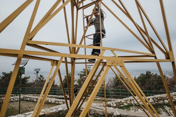 Individual engaging in an adventurous activity by climbing a metallic structure, with a cloudy sky...