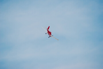 A vibrant red airplane performs an aerial maneuver in a bright blue sky, showcasing its dynamic...