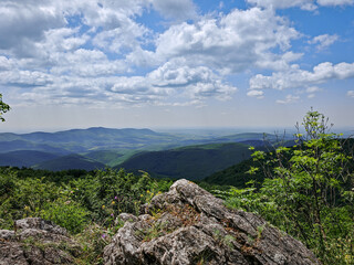 Wide-angle view from Pes-kő in the Bükk Mountains, overlooking the lush green ridges and the valley below, with Eger and Felsőtárkány visible in the distance.