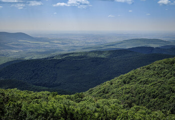 Distant view from Pes-kő in the Bükk Mountains toward Felsőtárkány and the town of Eger, with layered green forest ridges under a clear summer sky.