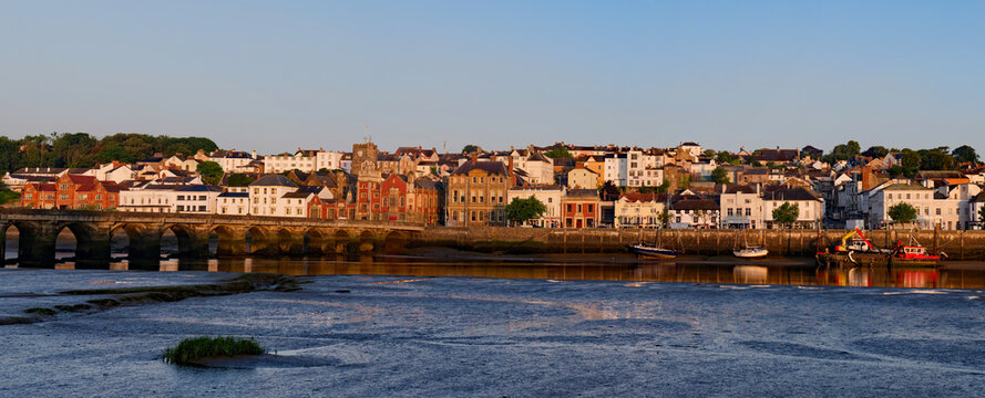 Bideford town with historic stone bridge at sunrise. River Torridge with boats at low tide. Wide view of old port town in Devon early in the morning. Town council building next to the church.