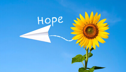 White paper airplane flying in bright blue sky with smoke trail writing the word hope and a blooming sunflower floating nearby
