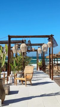 Rustic beach caf&eacute; with bamboo chairs and wooden lampshades in sunny Puglia, southern Italy. Tropical flowers sway in the sea breeze, capturing Mediterranean coastal charm