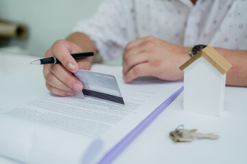 Businessperson signing real estate contract while holding credit card, representing property...