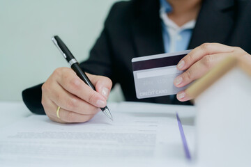 Businessperson signing real estate contract while holding credit card, representing property...