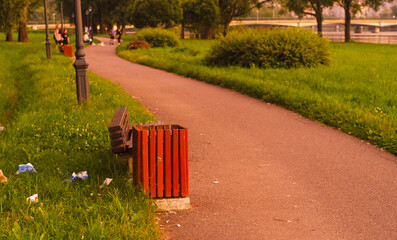 Trash can and scattered garbage nearby in the park on sunset.