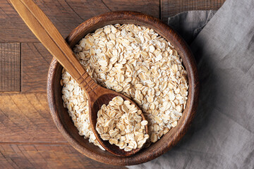 Rolled oats, uncooked oatmeal in wooden bowl, closeup view texture, healthy diet food