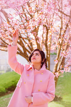 Portrait of a beautiful woman in pink coat under cherry blossoms in spring