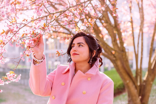 Portrait of a beautiful woman in pink coat under cherry blossoms in spring