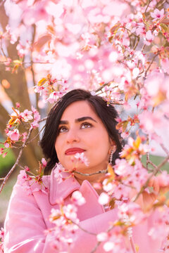 Portrait of a beautiful woman in pink coat under cherry blossoms in spring