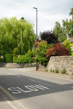 Baslow, The Peak District, England - July 14 2025: Scenic view of a quaint village street with a stone wall and lush greenery.