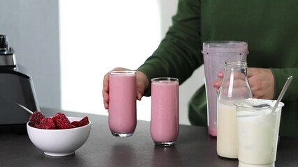 Close up of a woman in green sweater preparing fresh strawberries smoothie with yogurt and milk in the kitchen  - Powered by Adobe
