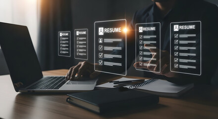 Man reviews resumes on a laptop with holographic displays, surrounded by a notebook and pen.