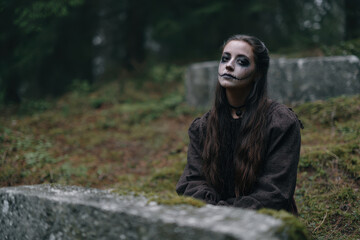 Girl with skeletal ghost makeup sits in misty forest, creating eerie atmosphere