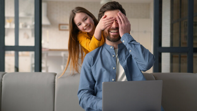 Mischievous positive Caucasian schoolgirl girl kid run surprise little daughter child close eyes hands happy parent man father work laptop remote job at home male guy dad laugh bonding family custody - Powered by Adobe