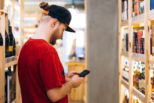 Man choosing alcohol in store while searching on smartphone.