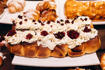 Fresh cinnamon rolls with white cream and jam in bakery display.